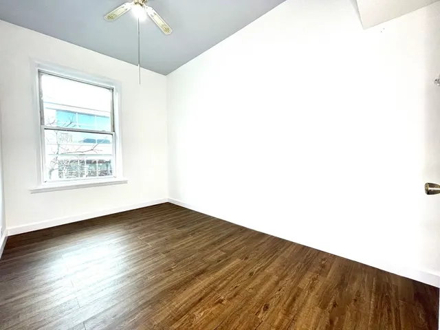 an empty room with wooden floor chandelier fan and windows