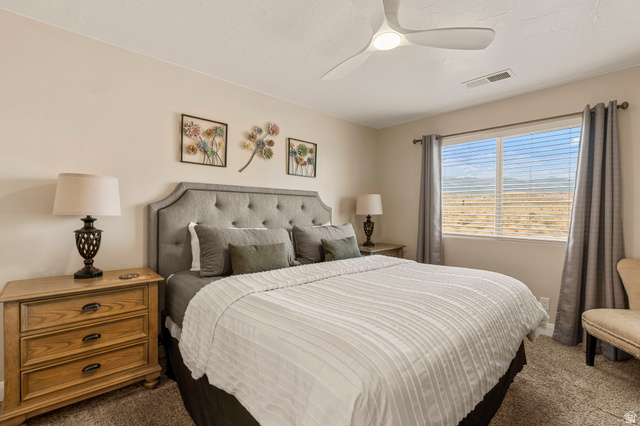 4257 Razor Drive Washington, UT 84780 - Photo 39 of 58 Bedroom featuring a tufted upholstered headboard, a ceiling fan with integrated lighting, a large window with blinds, and neutral carpeting