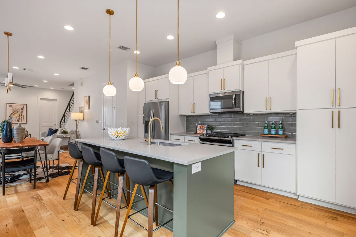 Modern kitchen showcasing a spacious quartz island with seating, brass-accented pendant lighting, stainless steel appliances, and crisp white cabinetry with gold hardware