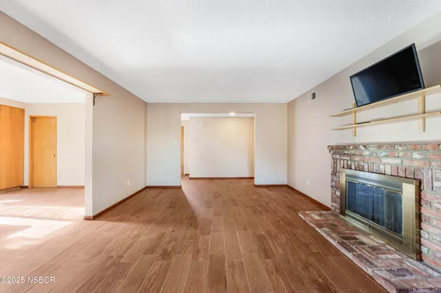 an empty room with wooden floor fireplace and windows