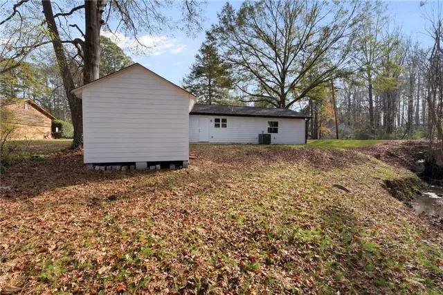 a view of a small white house with a large tree and wooden fence