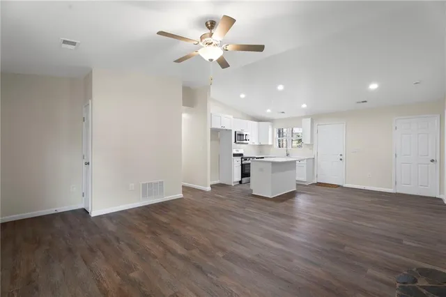 a view of an empty room with wooden floor and a ceiling fan