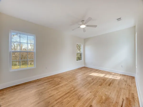 an empty room with wooden floor ceiling fan and windows