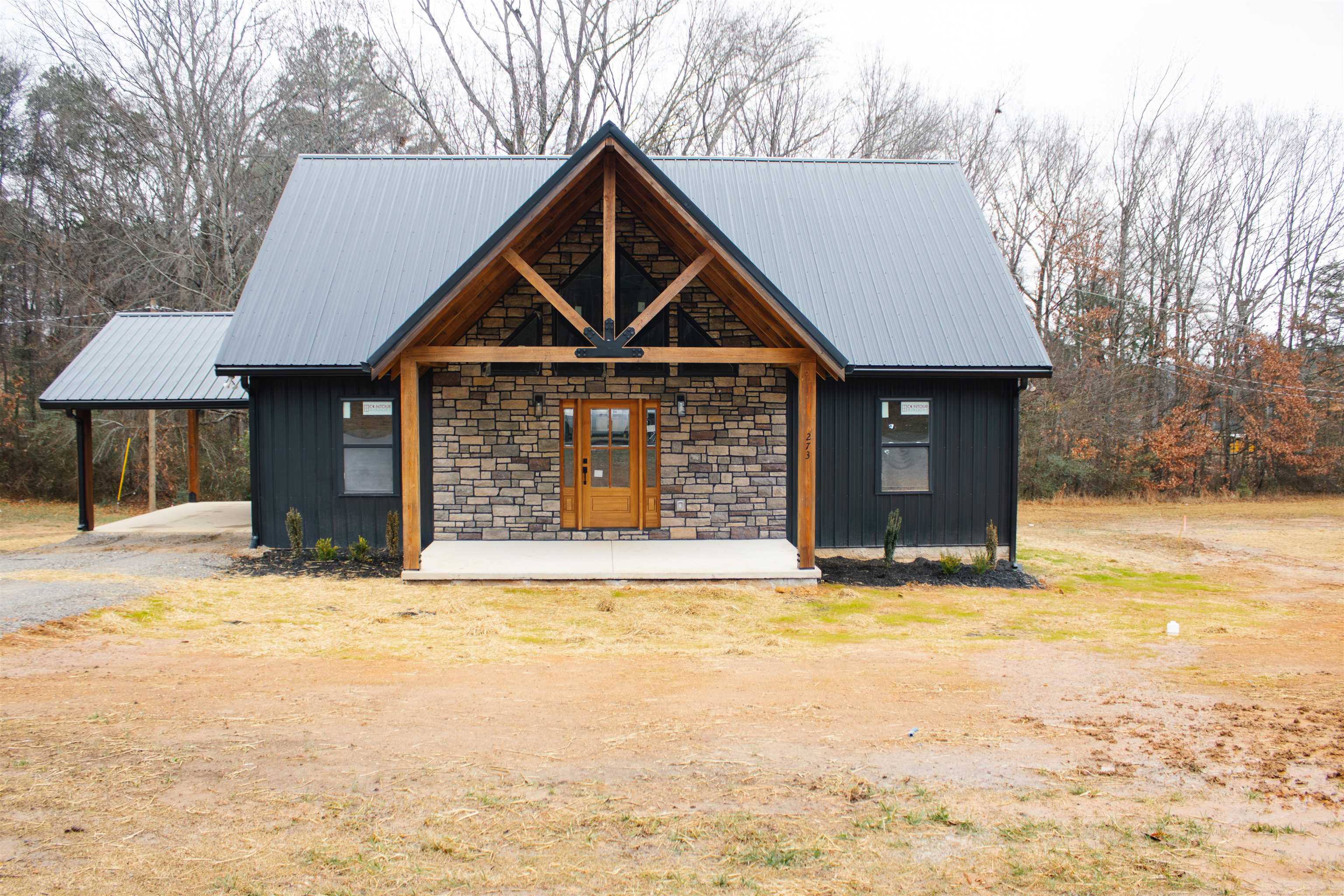 View of front of house with stone siding, a metal roof, a carport, and board and batten siding