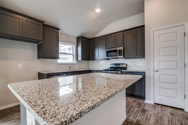 a kitchen with kitchen island granite countertop a sink dishwasher stove and microwave with wooden floor