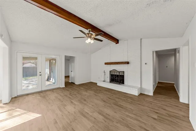 a view of an empty room with wooden floor fireplace and a window