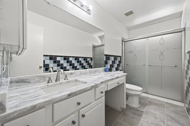 a bathroom with a granite countertop sink a toilet a mirror and shower