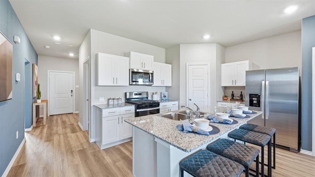 a kitchen with stainless steel appliances granite countertop a refrigerator a stove a sink a dining table and chairs with wooden floor