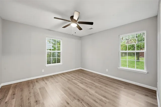 an empty room with wooden floor fan and windows