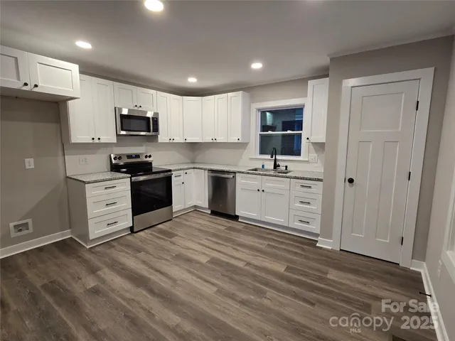 a kitchen with stainless steel appliances granite countertop a stove top oven a sink dishwasher and a refrigerator with wooden floor