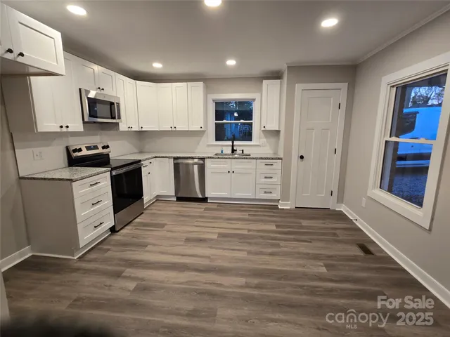 a large kitchen with stainless steel appliances granite countertop a stove top oven a sink dishwasher and a refrigerator with wooden floor