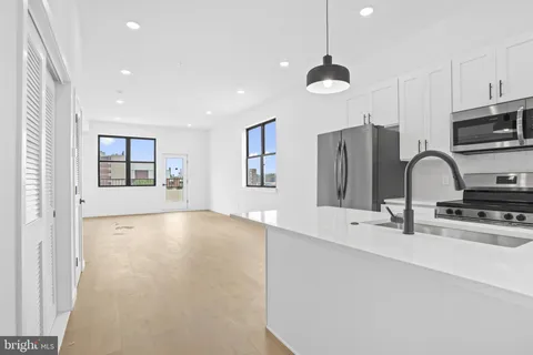 a view of a kitchen with stainless steel appliances a sink dishwasher a refrigerator and a stove with wooden floor