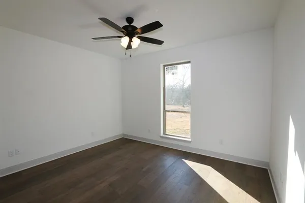 an empty room with wooden floor fan and windows