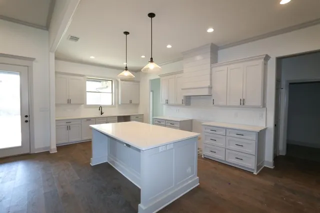 a large kitchen with kitchen island a sink dishwasher a stove a refrigerator and white cabinets with wooden floor