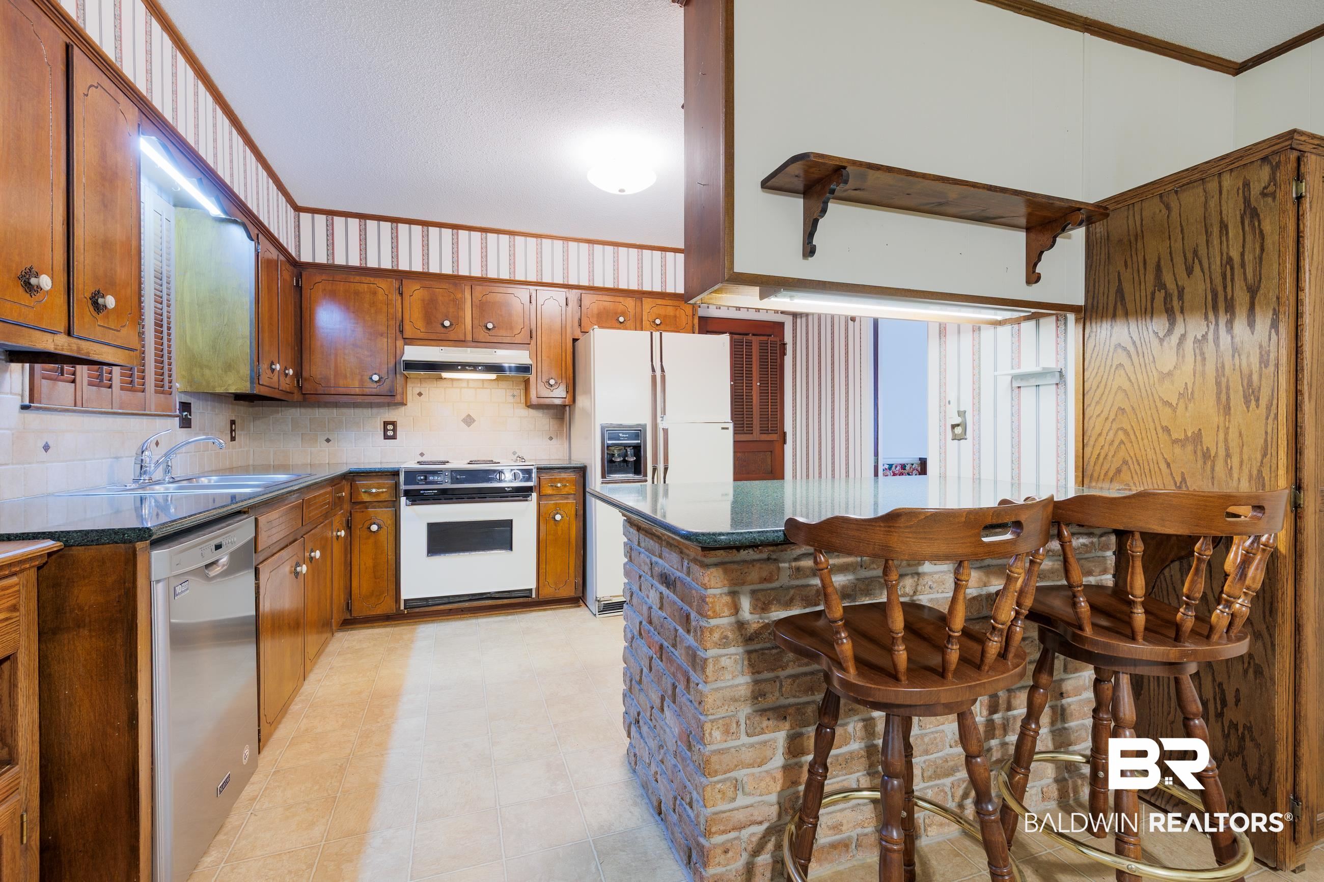 1367 Spring Valley Court Mobile, AL 36693 - Photo 5 of 29 Kitchen featuring wood cabinetry, dark countertops, a tile backsplash, and a brick-faced island with seating