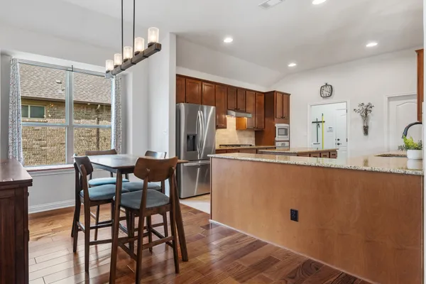 a kitchen with stainless steel appliances granite countertop a dining table chairs refrigerator sink and cabinets