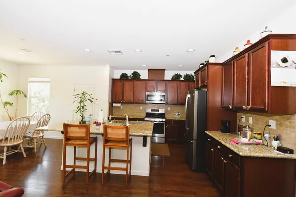 a kitchen with stainless steel appliances kitchen island granite countertop a stove a refrigerator a kitchen island a dining table and chairs with wooden floor