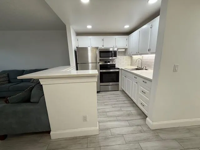 a kitchen with stainless steel appliances kitchen island granite countertop a refrigerator a stove a sink and white cabinets