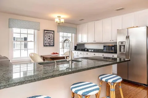 a kitchen with stainless steel appliances granite countertop a stove top oven a sink a dining table and chairs with wooden floor