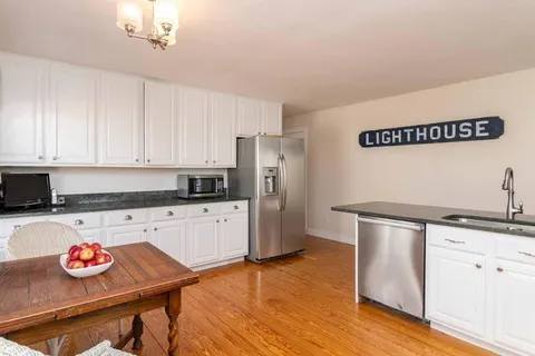 a kitchen with stainless steel appliances granite countertop a sink dishwasher a stove a refrigerator and white cabinets with wooden floor