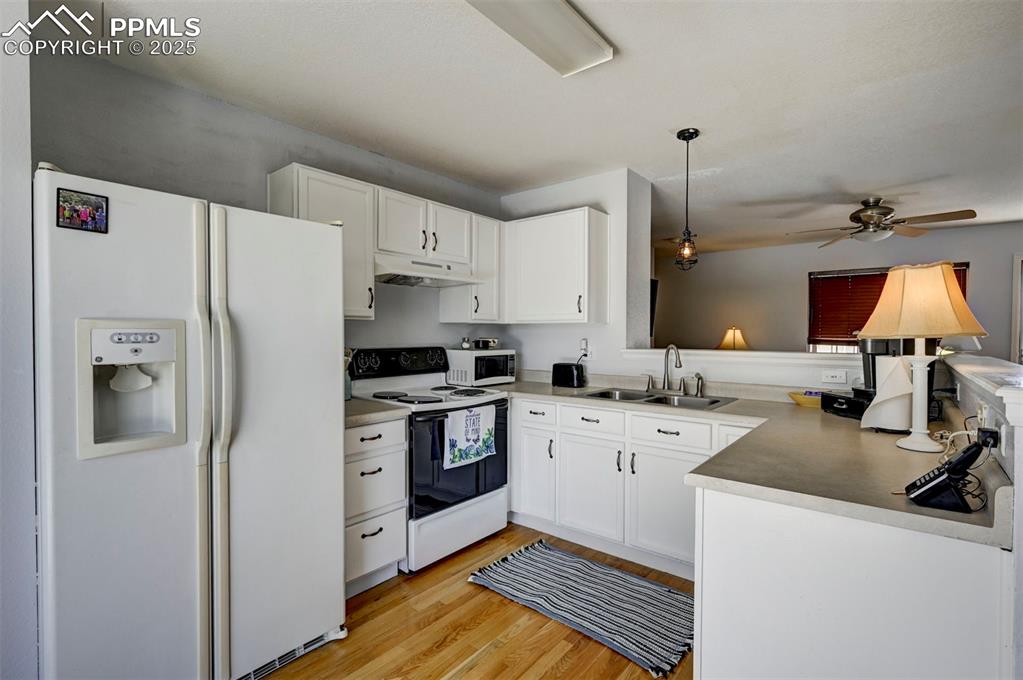12593 Pine Valley Circle Peyton, CO 80831 - Photo 6 of 17 Kitchen with white appliances, under cabinet range hood, a ceiling fan, light wood finished floors, and white cabinets