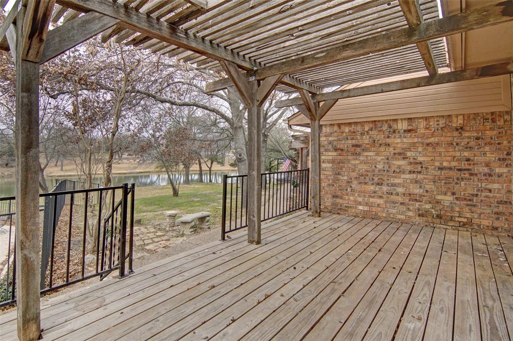 Back deck with black aluminum fencing, a pergola, and a beautiful treed view of duck pond with a fountain.