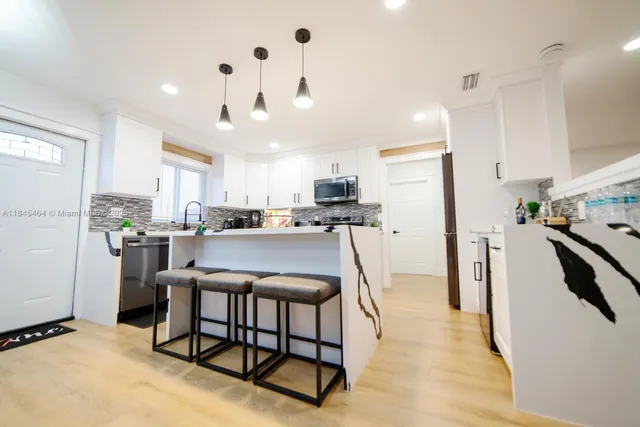 a kitchen with stainless steel appliances kitchen island granite countertop a refrigerator a stove a sink dishwasher and white cabinets with wooden floor