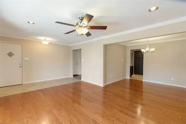 a view of an empty room with wooden floor and a ceiling fan