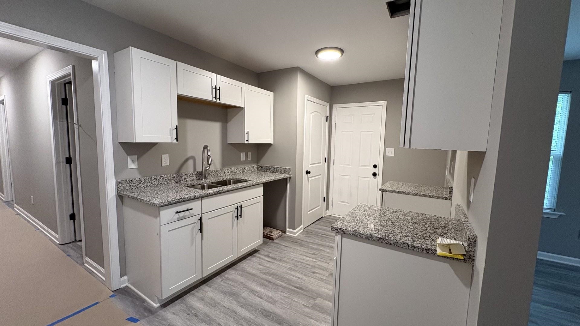 643 Kent Street Memphis, TN 38111 - Photo 8 of 14 Contemporary kitchen featuring white cabinetry, light-toned granite-style countertops, stainless steel sink with a gooseneck faucet, and wood-finish flooring