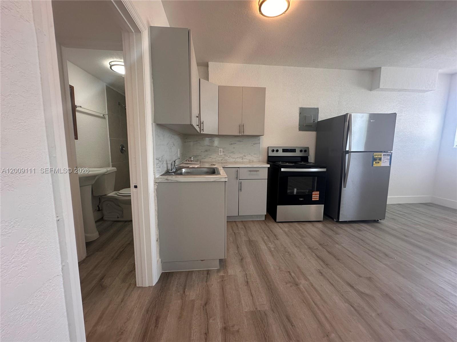 50 Northwest 79th Street, Unit 6 Miami, FL 33150 - Photo 11 of 30 a kitchen with a refrigerator a stove top oven and wooden floor