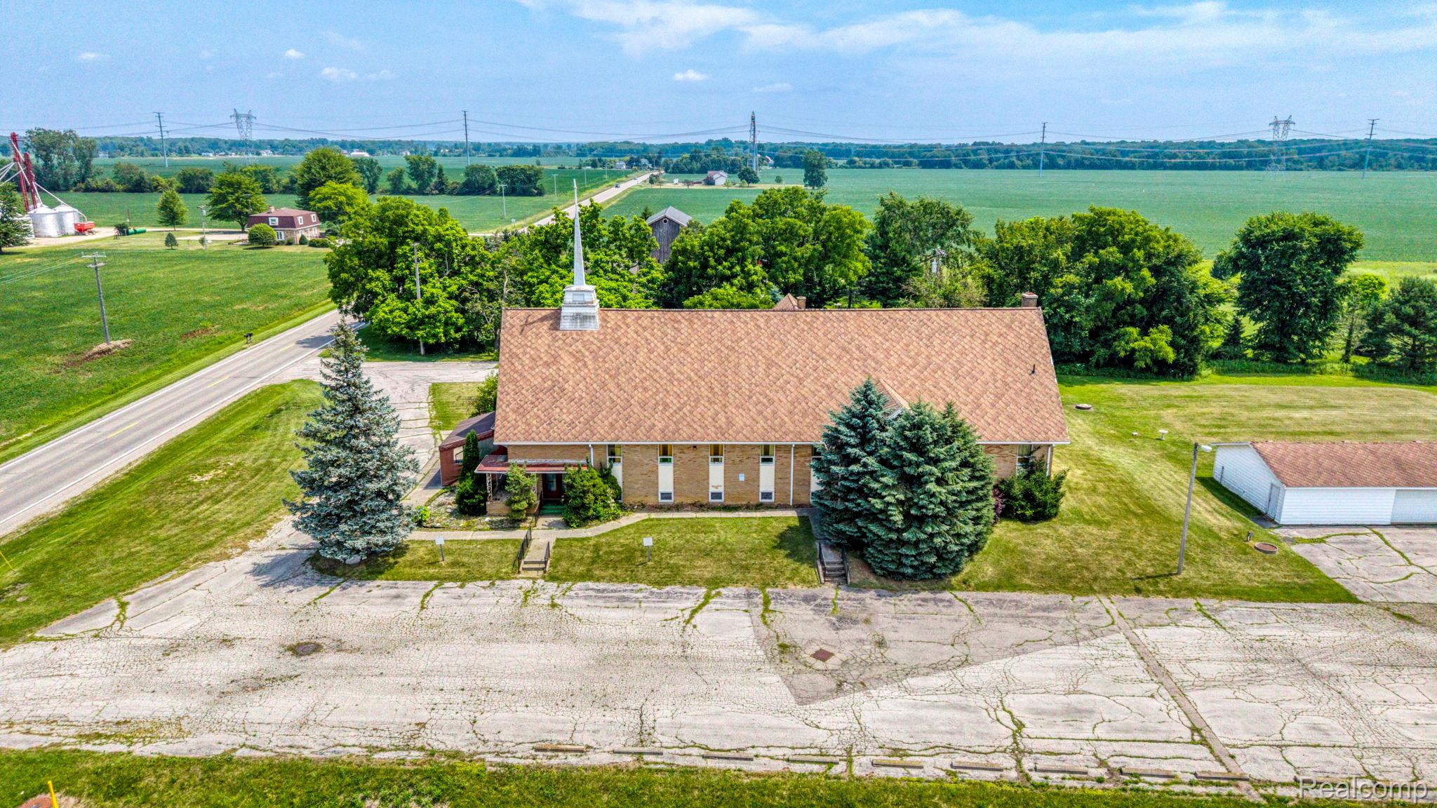 9735 Dolan Road Columbus, MI 48063 - Photo 7 of 63 Brick building with a steeple, set on a lot featuring mature evergreen trees and a paved parking area