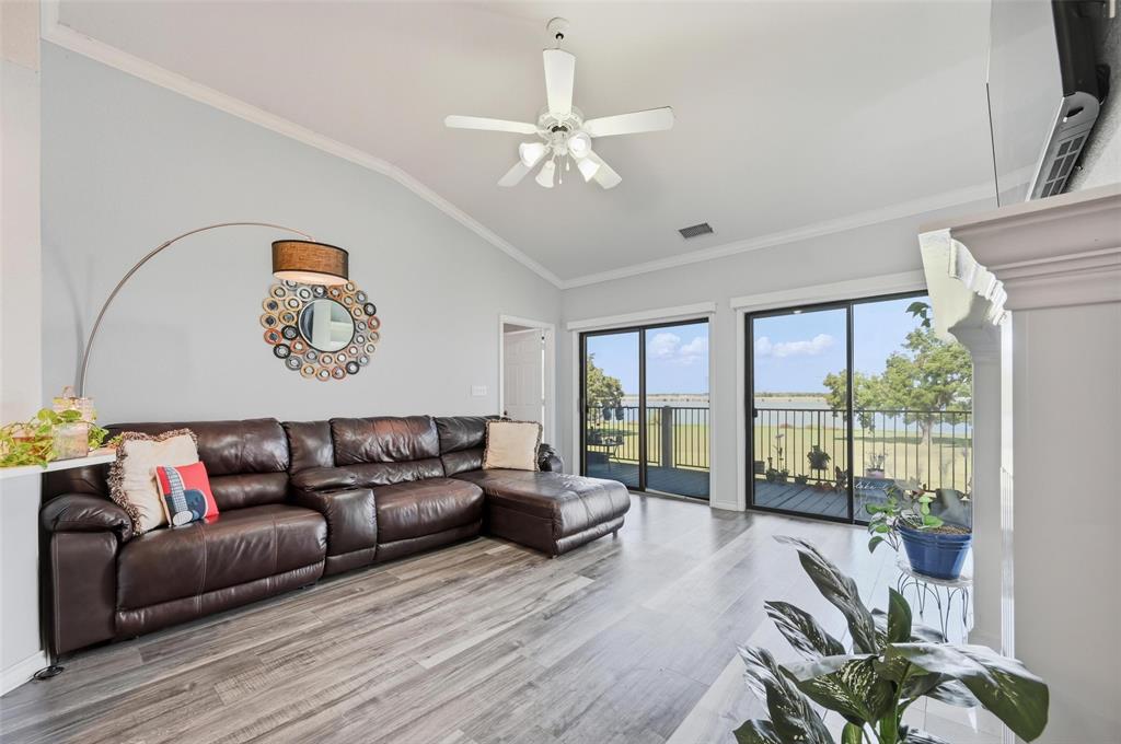 Living area with vaulted ceiling, ornamental molding, wood finished floors, ceiling fan, and a water view