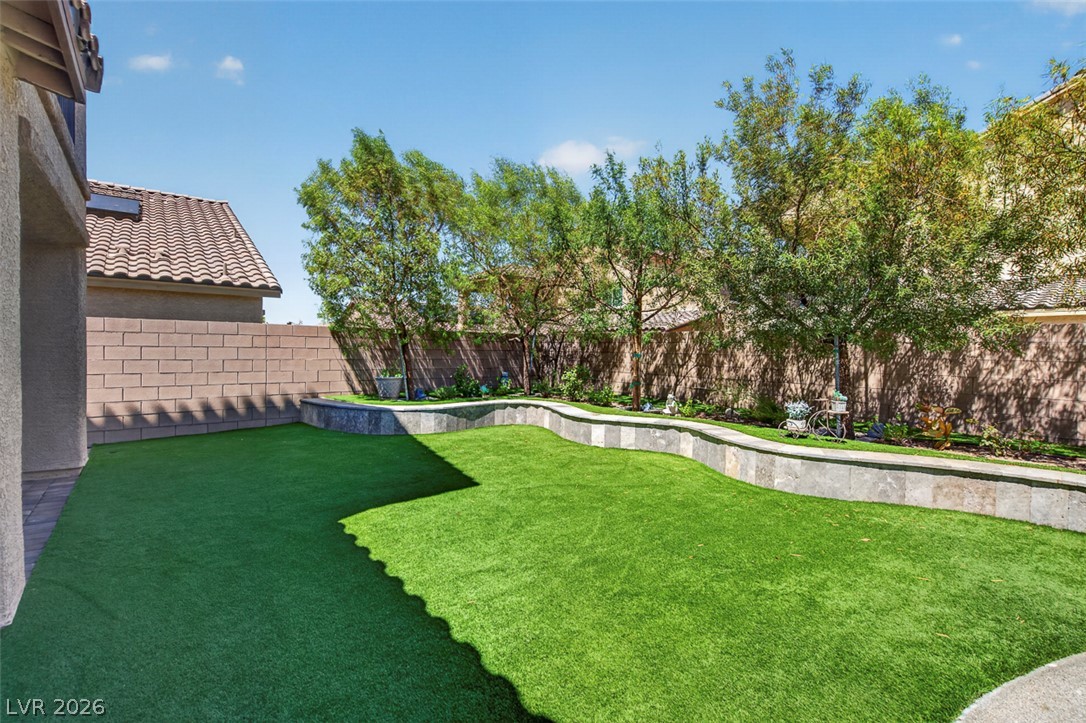 1824 Redland Ridge Street Henderson, NV 89002 - Photo 60 of 69 Green yard with manicured landscaping and a natural stone retaining wall, perfect for outdoor enjoyment.