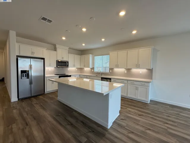 a large kitchen with kitchen island a sink dishwasher a refrigerator and white cabinets with wooden floor