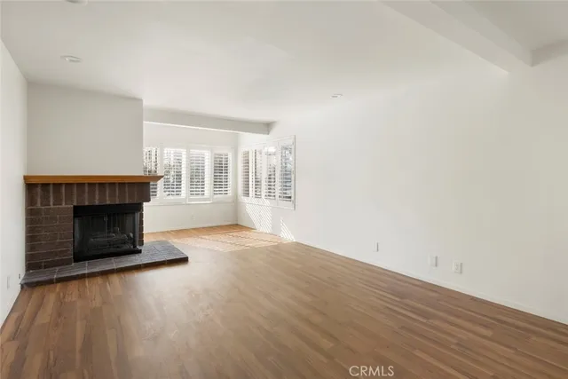 a view of an empty room with wooden floor fireplace and a window