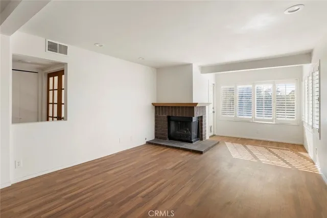 a view of an empty room with wooden floor fireplace and a window