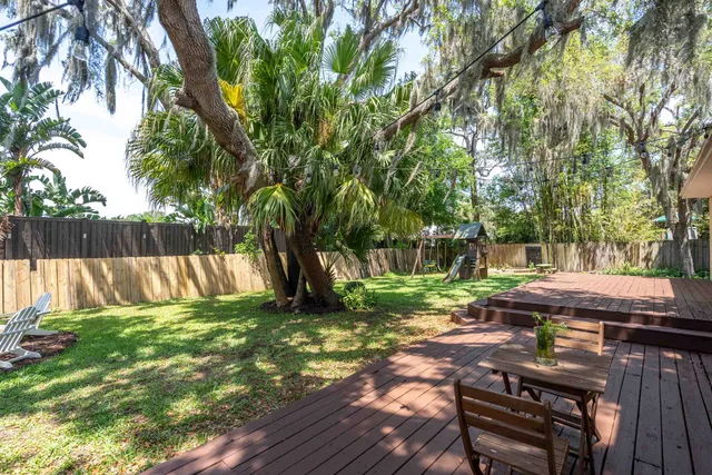 a view of a backyard with table and chairs a barbeque and a large trees with wooden fence