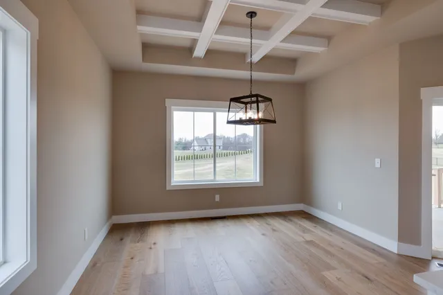 an empty room with wooden floor chandelier and windows