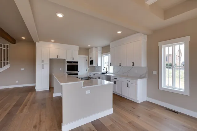 a large white kitchen with stainless steel appliances kitchen island a large counter top and a wooden floors