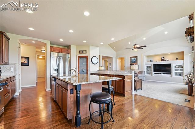1918 Bashley Road Monument, CO 80132 - Photo 14 of 48 Kitchen with arched walkways, appliances with stainless steel finishes, wood finished floors, an island with sink, and a kitchen bar