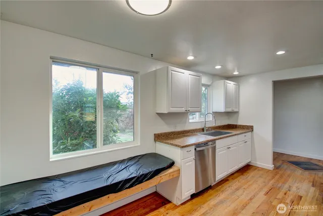 a kitchen with stainless steel appliances granite countertop a stove a sink and white cabinets with wooden floor