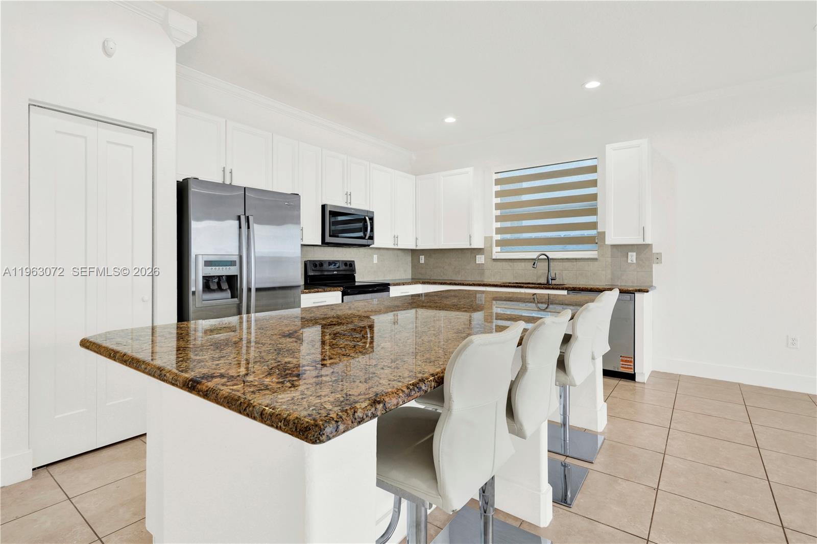 23824 Southwest 107th Place Homestead, FL 33032 - Photo 8 of 33 a kitchen with kitchen island granite countertop a table chairs microwave and refrigerator