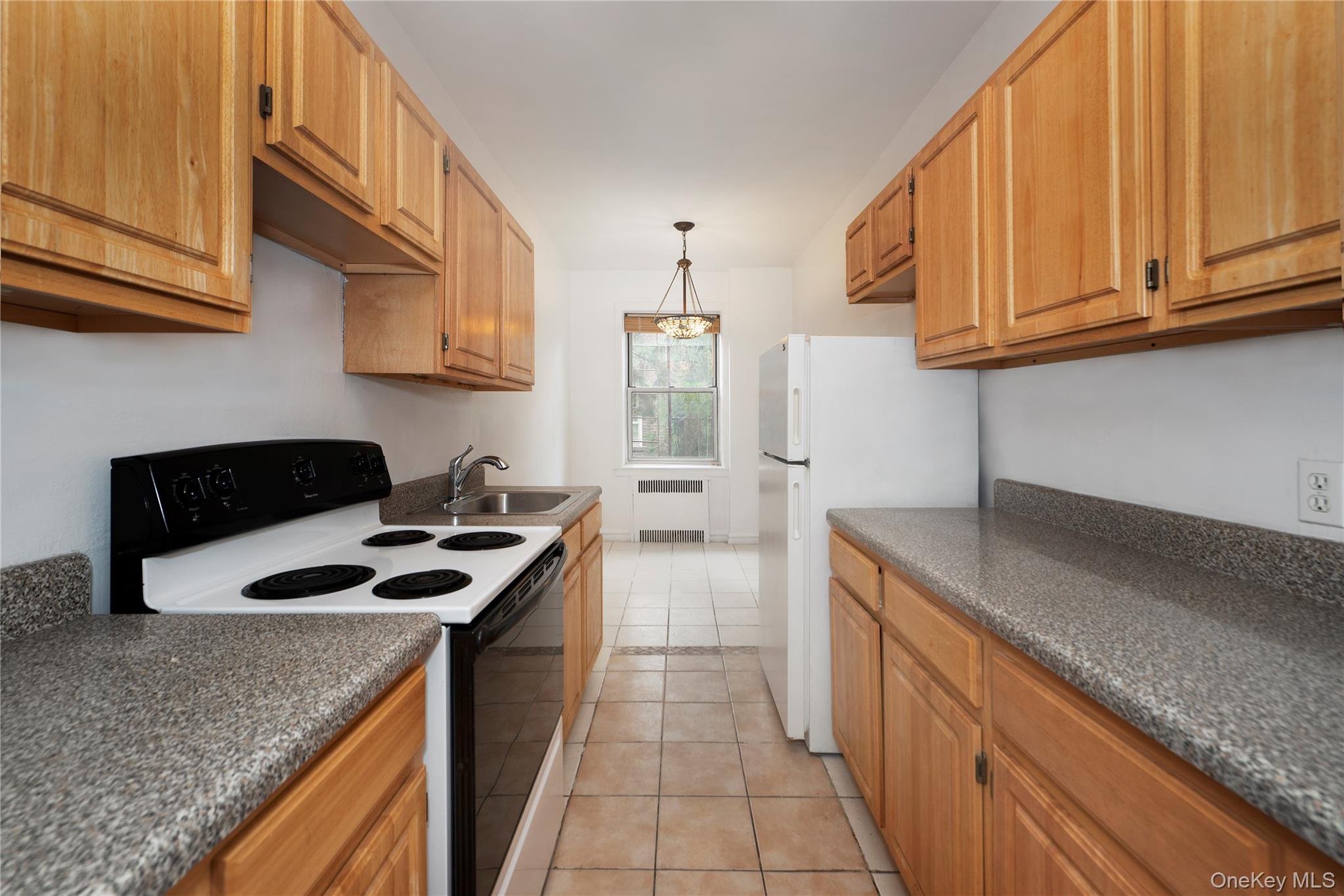 86-10 34th Avenue, Unit 225 Queens, NY 11372 - Photo 4 of 11 Kitchen with range with electric stovetop, light tile patterned floors, decorative light fixtures, freestanding refrigerator, and radiator heating unit