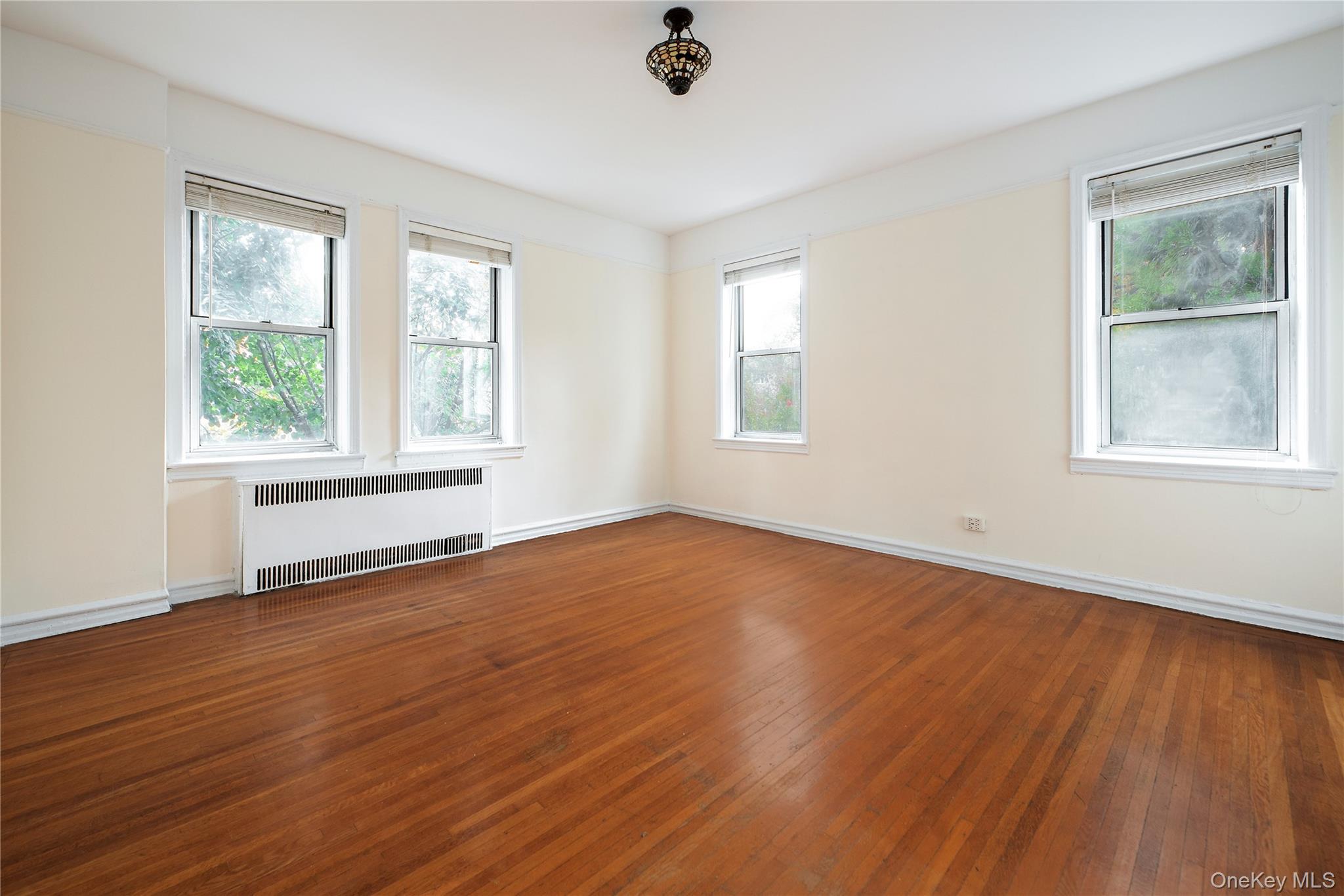 86-10 34th Avenue, Unit 225 Queens, NY 11372 - Photo 7 of 11 Spare room featuring radiator heating unit, hardwood / wood-style floors, and healthy amount of natural light
