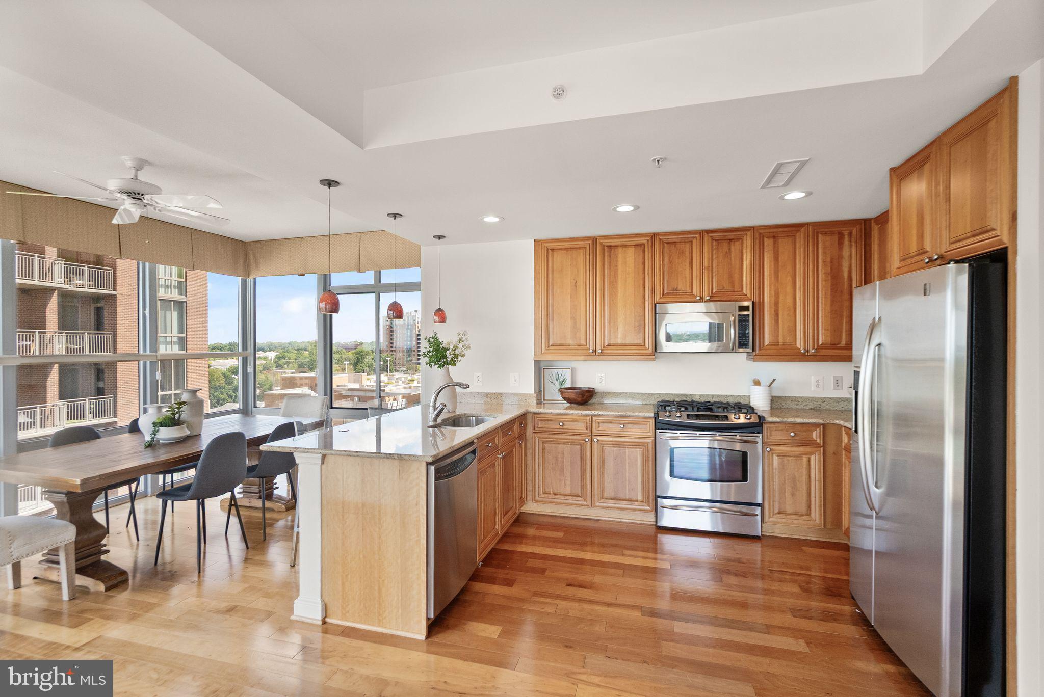 11990 Market Street, Unit 1015 Reston, VA 20190 - Photo 21 of 90 a kitchen with stainless steel appliances granite countertop a stove top oven a refrigerator a sink and dining table with wooden floor