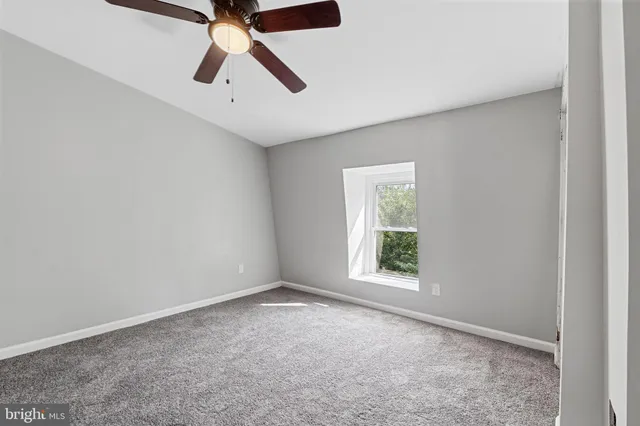 an empty room with chandelier fan and windows