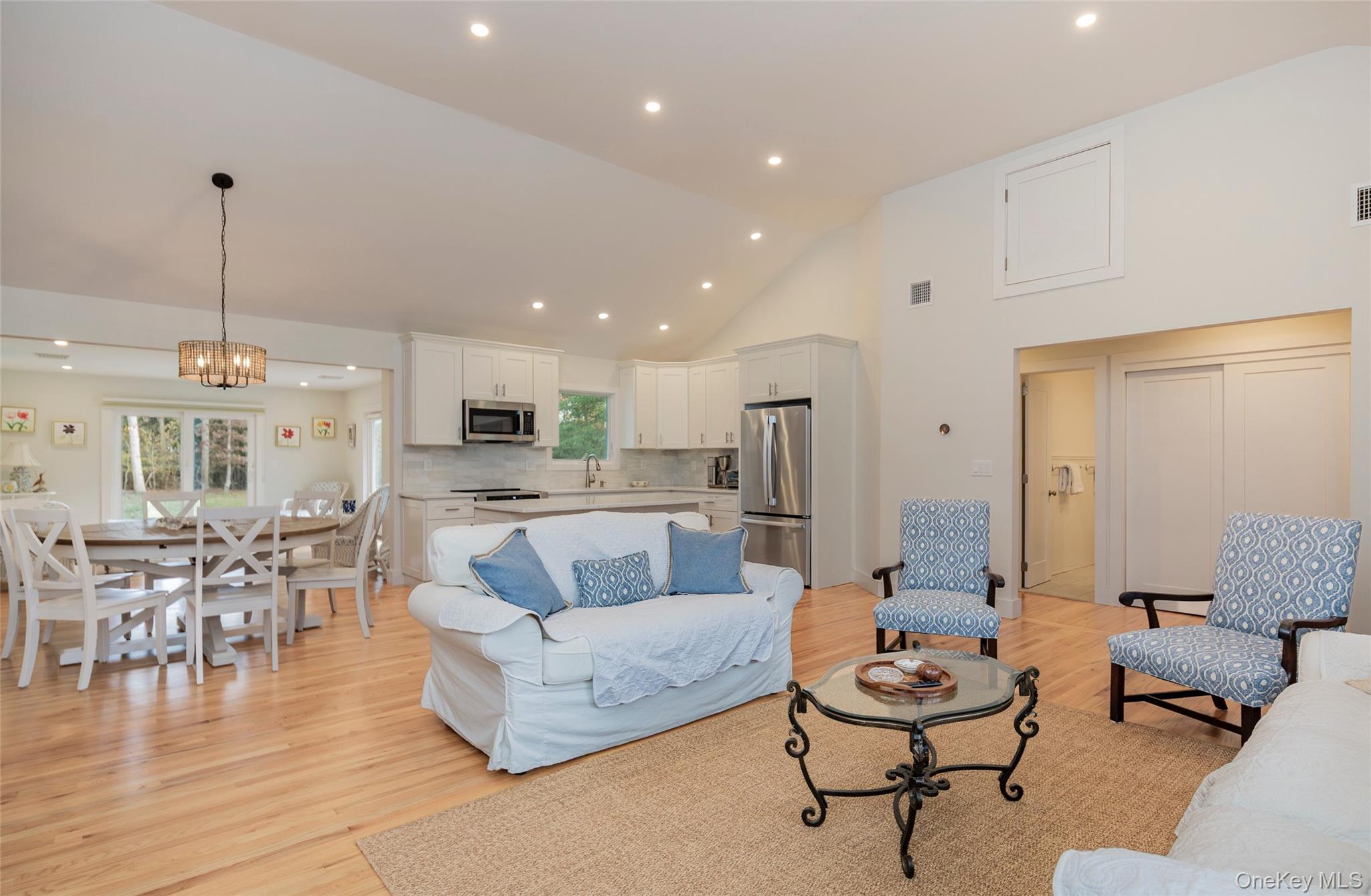 Living area with light wood finished floors, high vaulted ceiling, a chandelier, and recessed lighting
