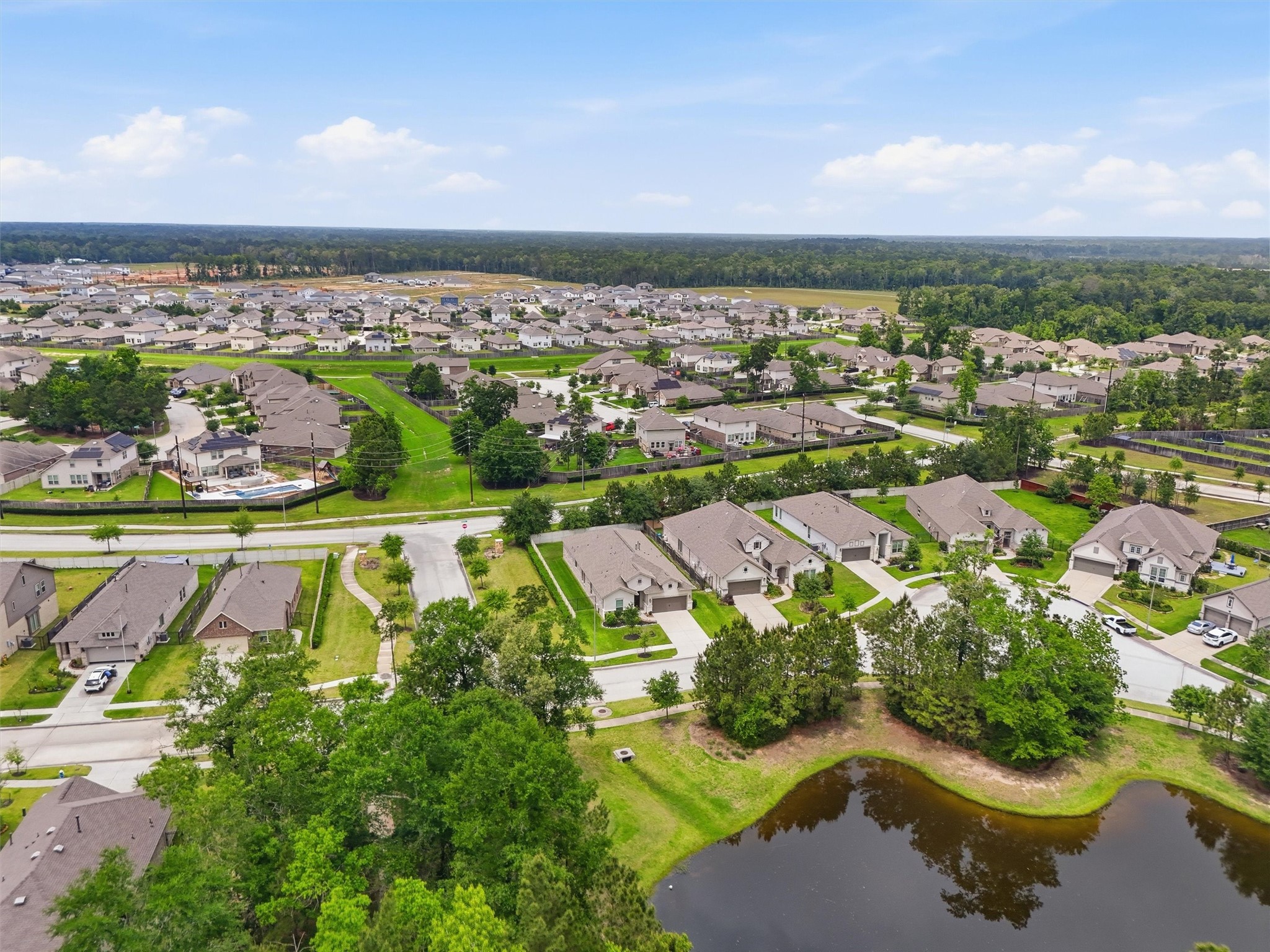 6071 Windward Falls Way Porter, TX 77365 - Photo 32 of 33 This aerial photo showcases a peaceful suburban neighborhood with neatly arranged homes, lush greenery, and a small pond. The area is surrounded by trees, offering a serene and natural setting.