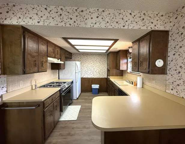 a large kitchen with stainless steel appliances a stove a sink dishwasher and a refrigerator with wooden floor