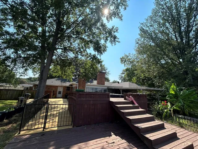 a view of house with deck outdoor seating and trees in the background